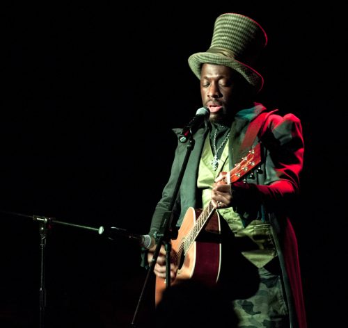 photograph of man in green hat and suit playing the guitar
