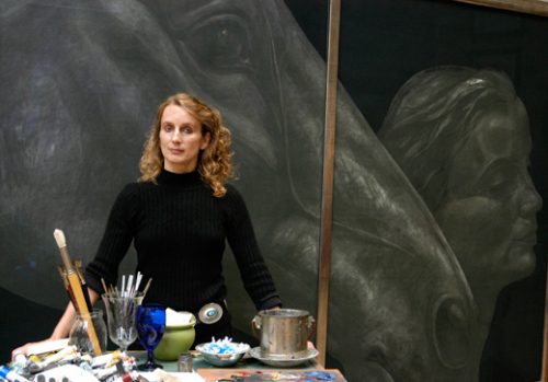 Photograph of Emma Sargeant, painter in her studio with painting of horse in the background